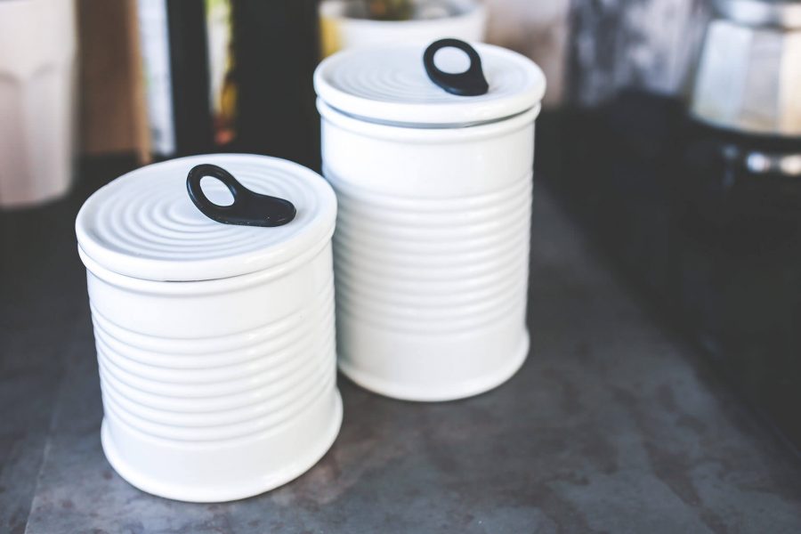Two white ribbed ceramic canisters with black ring handles on a kitchen countertop.