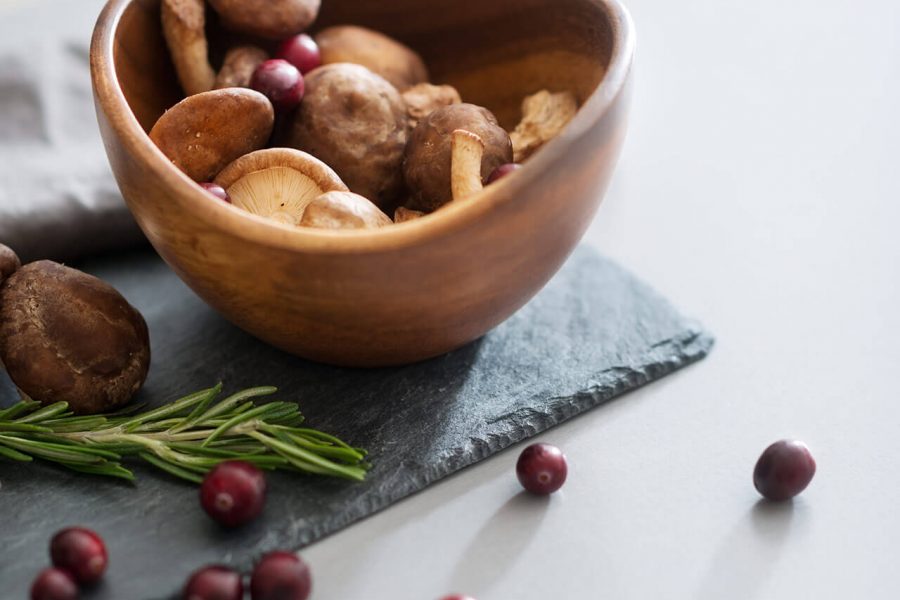 A wooden bowl filled with small potatoes on a slate board, garnished with rosemary and scattered cranberries on a white surface.
