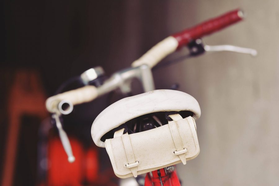 Close-up of a white bicycle saddle with a red frame and blurred background.