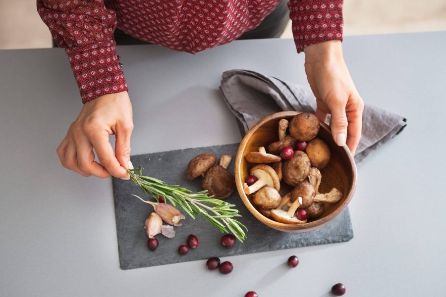 Person holding a bowl of fresh mushrooms and herbs over a slate serving board with scattered cherries.