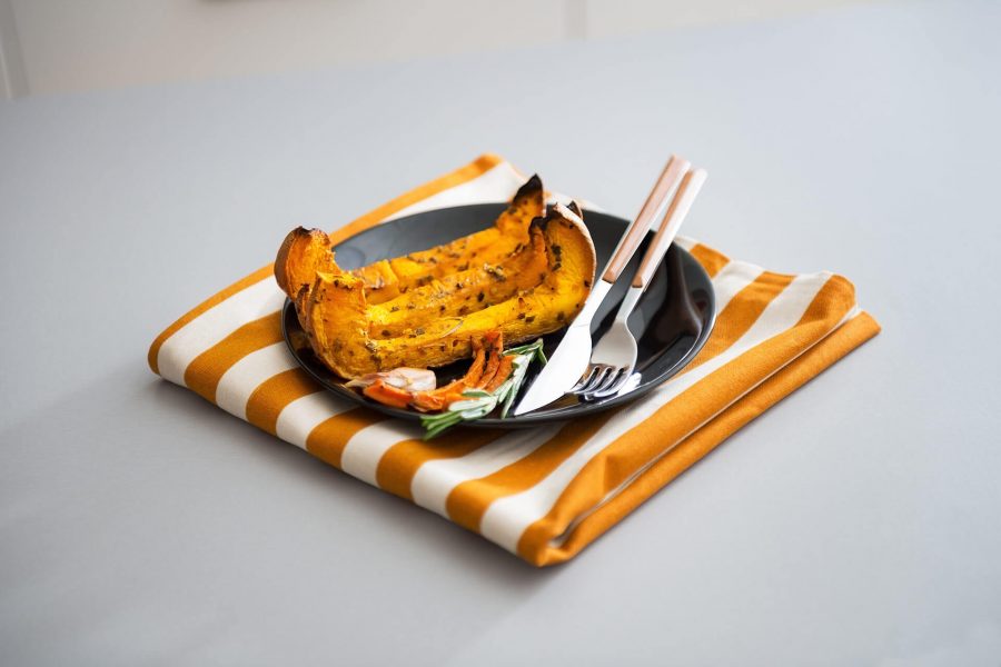 Grilled stuffed pumpkin served on a white plate with fork and knife, placed on a striped orange and white napkin.