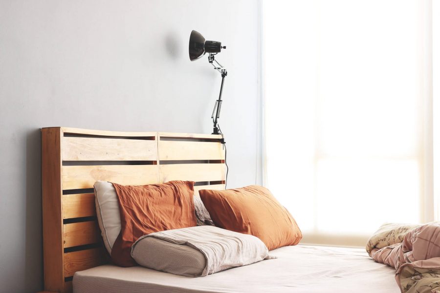 A cozy bedroom with a wooden headboard, orange pillows, and a black adjustable wall lamp on a white wall.