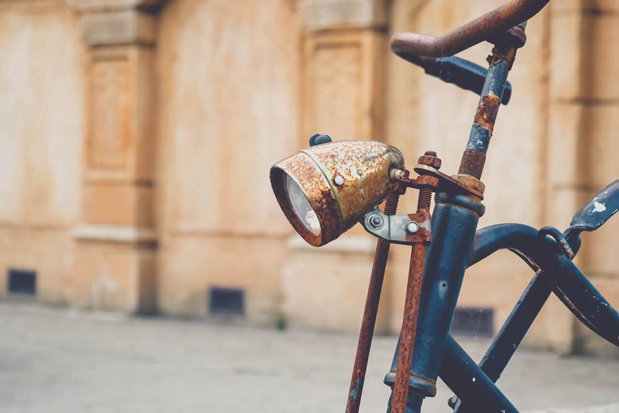Close-up of a vintage bicycle with a woven wicker basket attached to the handlebars against a stone wall backdrop.