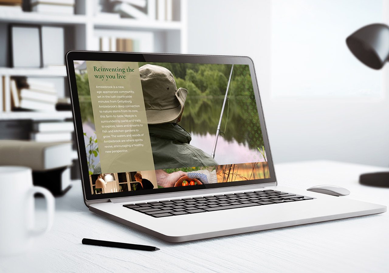 A laptop on a desk displaying a website with a hat and scenic nature image, surrounded by office supplies and a plant.