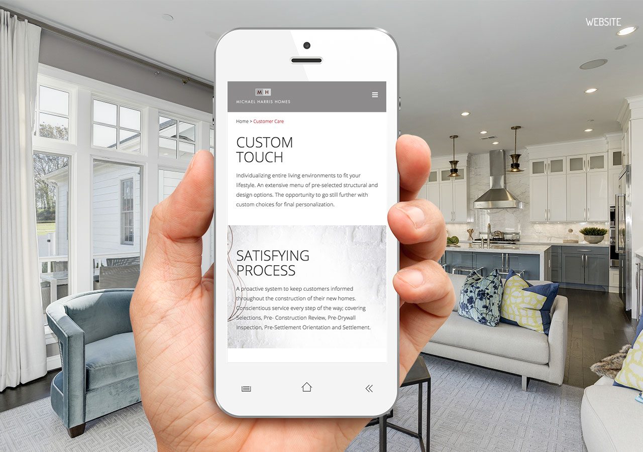 A hand holding a smartphone displaying a webpage about custom touch and satisfying process in a modern kitchen setting.