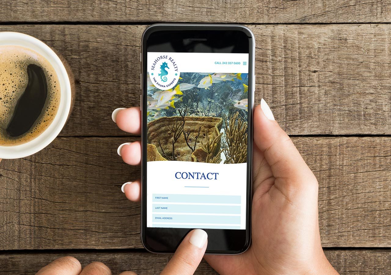A person holding a smartphone displaying a website contact page with a nature-themed background on a wooden table.