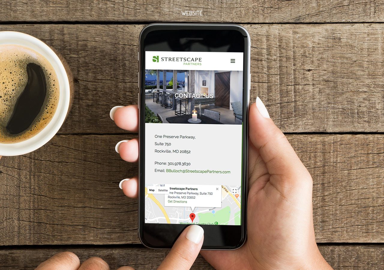 A hand holding a smartphone displaying a map and directions on a wooden table with a coffee cup nearby.