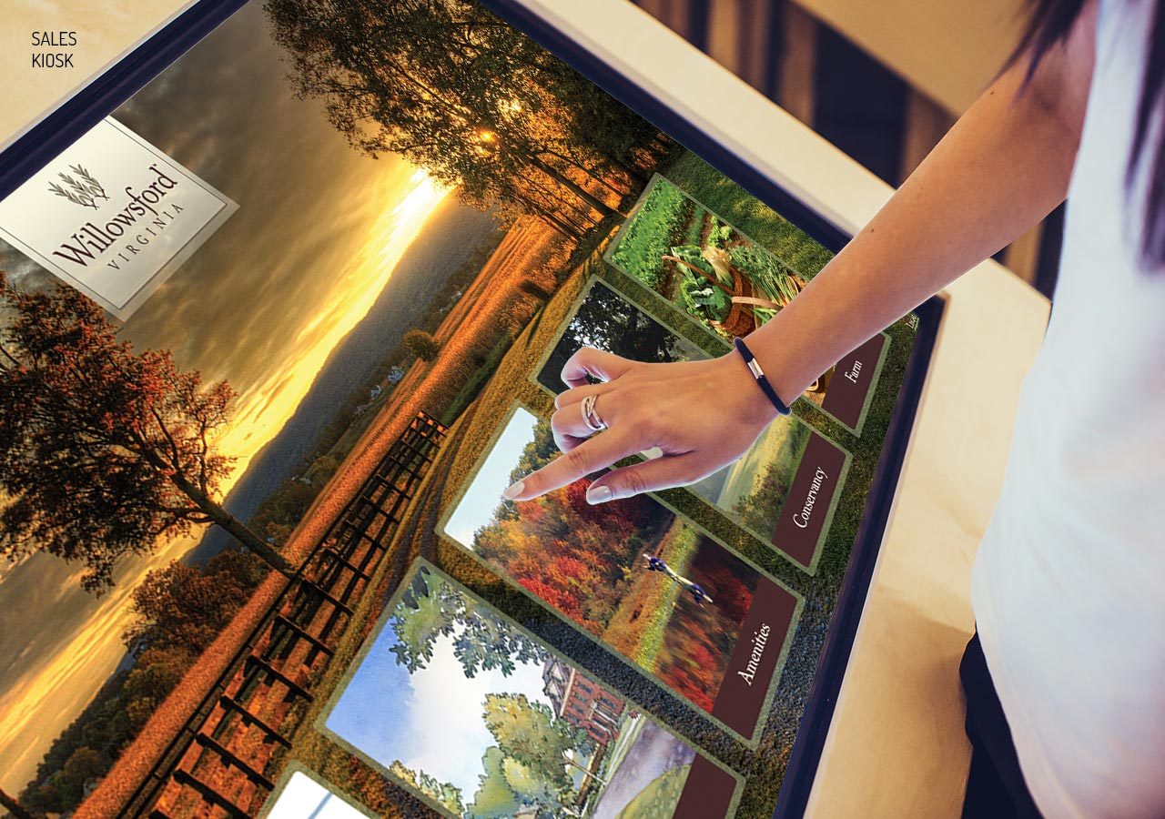 A person interacting with a touchscreen display featuring multiple landscape images and a scenic sunset photo.